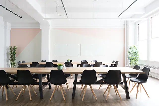 A bright, empty modern meeting area with long tables, chairs and large windows in a commercial office.
